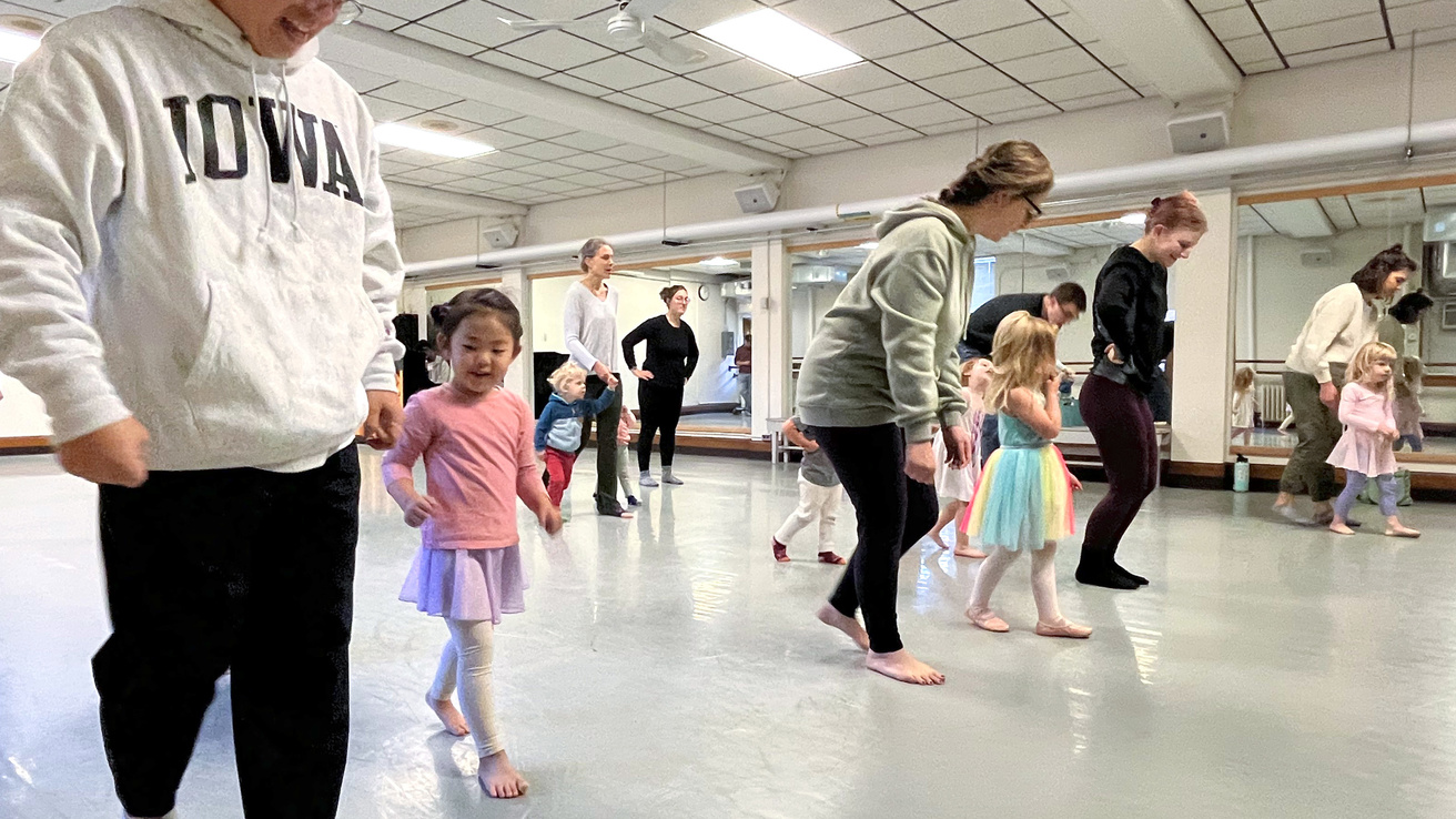 Parents and young children travel across a dance studio floor together